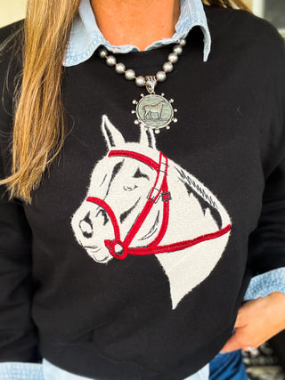 Black sweater with a horse design worn by a person, with a pearl necklace visible.