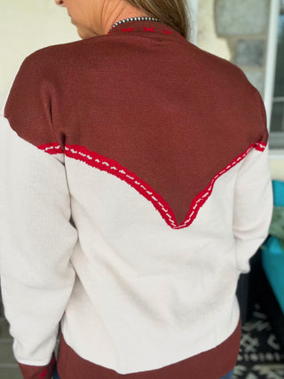 Person wearing a white sweater with a maroon collar and trim.