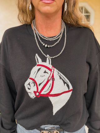 Person wearing a black sweatshirt with a horse design, standing indoors.