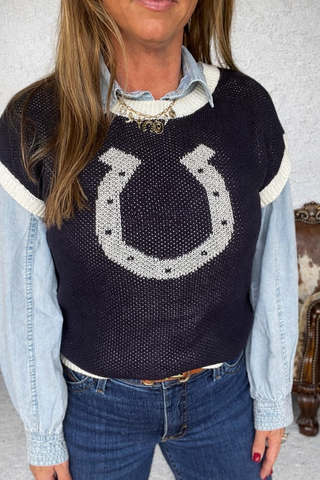 Person wearing a navy sweater with a horseshoe design, light blue shirt, and jeans.